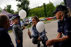 Dziecko z balonikiem w ręku, kobieta obok dziecka i dwoje policjantów po bokach