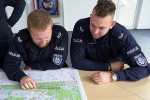 Policjanci podczas szkolenia siedzą w sali, a na biurku mają rozłożoną mapę