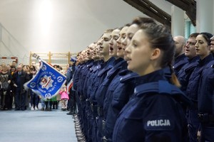 Ślubujący policjanci stojący w szeregu i sztandar KWP w Olsztynie w tle