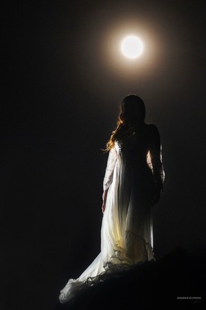 Kobieta w mroku w białej sukni i księżyc nad jej głową
