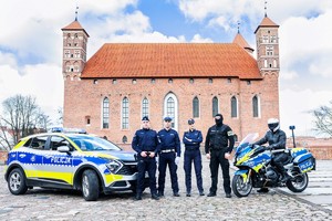 Zdjęcie radiowozu, policjantów i motocykla na tle zamku