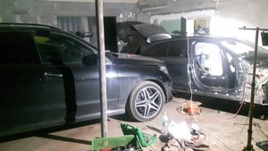 Fotografia kolorowa. Przedstawia wnętrze garażu, a w nim dwa odzyskane samochody. Jeden z pojazdów jest częściowo rozmontowany. Na posadzce narzędzia.