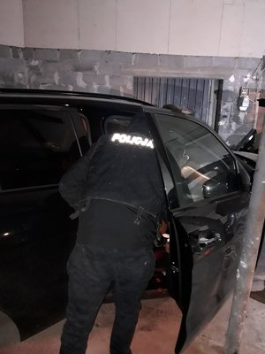 Fotografia kolorowa. Przedstawia wnętrze garażu, a w nim odzyskany samochody, przy otwartych drzwiach pojazdu stoi policjant..