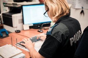 pomieszczenie biurowe, policjantka w trakcie pisania na klawiaturze komputera