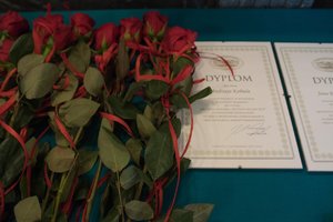 Zdjęcie kolorowe. Widoczne kwiaty, oraz dyplomy dla osób wyróżnionych.