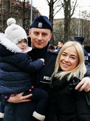 Policjant trzyma na ręku dziecku, obok stoi jego partnerka.