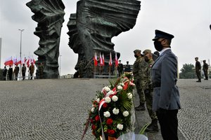 Przedstawiciele służb mundurowych stoją z wieńcami kwiatów przed Pomnikiem Powstańców Śląskich