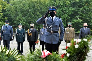 Przedstawiciele służb mundurowych, w tym Zastępca Komendanta Wojewódzkiego Policji stoją przed Pomnikiem Powstańców Śląskich, policjant, który złożył wieniec oddaje honor