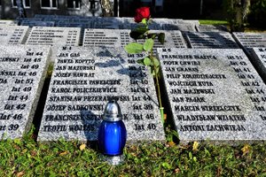 Niebieski znicz i czerwona róża przy płycie z imionami i nazwiskami zmarłych i pomordowanych policjantów