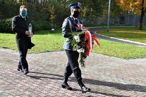 gen. bryg. w st. spocz. dr Tomasz Miłkowski trzymający zapalony znicz idzie za umundurowanym policjantem z asysty honorowej, który niesie wieniec kwiatów