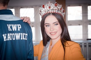 Zdjęcie kolorowe. Widoczna Miss Polski 2020 oraz plecy policjanta z bluza z napisem KWP Katowice na terenie hali sportowej. Autor zdjęcia: Michał Piątek