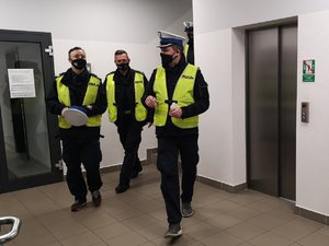 Zdjęcie zrobione w korytarzu bielskiej komendy. Przedstawia policjanta oraz dwóch kabareciarzy, wszyscy ubrani w policyjne mundury.