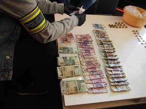Pieniądze rozłożone na stole i dłonie policjanta trzymającego banknoty
