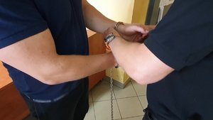 Policjant zakłada kajdanki na dłonie zatrzymanego.