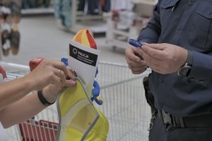 Zdjęcie kolorowe. Widoczny umundurowany policjant, który na terenie sklepu wręcza gadżet osobie