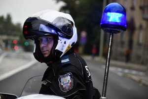 Policjant na motocyklu z kaskiem na głowie. Obok świecąca lampa błyskowa motocykla policyjnego.