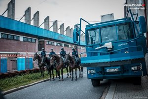 Policjanci policji konnej na koniach, podczas zabezpieczenia meczu. Z prawej strony fragment armaty wodnej.