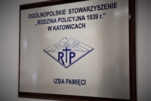 Tabliczka z napisem Ogólnopolskie Stowarzyszenie Rodzina policyjna 1939 rok w Katowicach. Pod nią znajduje się logo, a pod nim napis Izba Pamięci.