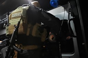 Na zdjęciu policyjny komandos w pełnym umundurowaniu z bronią przewieszoną przez ramię. Fotografia wykonana w policyjnym, nieoznakowanym radiowozie.