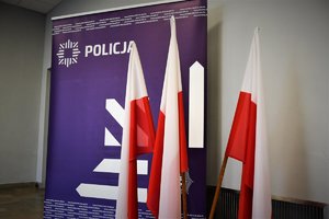 Flagi Polski, w tle baner z napisem i logo Policji.