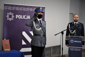 Dowódca uroczystości oraz policyjny lektor prowadzący uroczystość, w tle baner z napisem Policja.