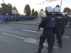 Widoczni umundurowani policjanci i radiowozy oraz kibice w drodze na mecz