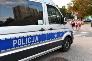 Oznakowany policyjny radiowóz przed przejściem dla pieszych. W tle kibice Polski.