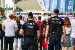 Zdjęcie kolorowe: dwóch umundurowanych policjantów wśród grupy kibiców pod katowickim spodkiem.