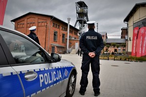 Na zdjęciu dwaj umundurowani policjanci i radiowóz na placu