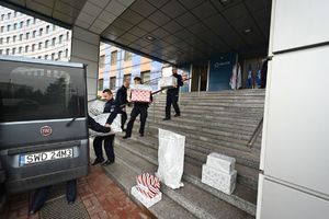 Policjanci znoszą spakowane paczki do samochodu przed komendą