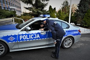 Policjant schyla się do okna radiowozu, za kierownicą którego siedzi Pani Iwona.