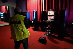Zdjęcie przedstawia wnętrze salonu gier, maszyny do gier oraz nieumundurowanego policjanta, który wykonuje czynności służbowe.
