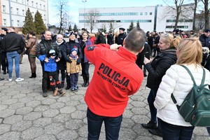 zdjęcie przedstawia policjant w czerwonym polarze robi zdjęcie stojącemu w tle nowemu policjantowi z rodziną