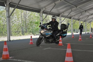 Zdjęcie. Policjant na motocyklu podczas konkurencji jazdy na motocyklu oraz inni umundurowani policjanci
