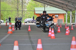 Zdjęcie. Policjant na motocyklu podczas konkurencji jazdy na motocyklu oraz inni umundurowani policjanci