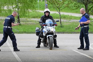 Zdjęcie. Policjant na motocyklu podczas konkurencji jazdy na motocyklu oraz inni umundurowani policjanci