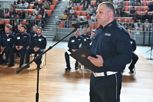 Zdjęcie. Umundurowany policjant przed mikrofonem hali sportowej