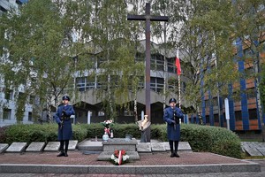 Zdjęcie. Warta honorowa dwóch umundurowanych policjantów z bronią długą przed Grobem Policjanta Polskiego, widoczny również grób i krzyż, w tle rotunda komendy