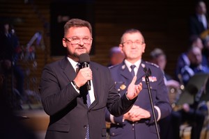 Na zdjęciu widać mężczyznę mówiącego do mikrofonu oraz policjanta w mundurze galowym