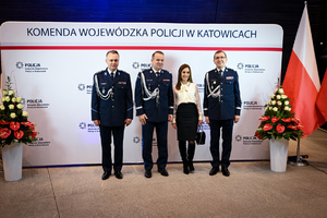 Zdjęcie przedstawia trzech policjantów oraz kobietę, osoby stoją przed napisem Komenda Wojewódzka Policji w Katowicach
