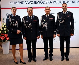 Zdjęcie przedstawia trzech policjantów i policjantkę, osoby stoją przed napisem Komenda Wojewódzka Policji w Katowicach