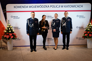 Zdjęcie przedstawia dwóch policjantów, policjantkę i kobietę, osoby stoją przed napisem Komenda Wojewódzka Policji w Katowicach