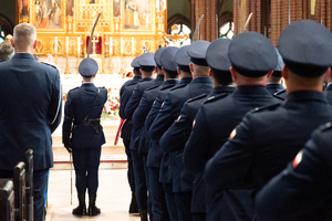 kolorowe zdjęcie wykonane za plecami policjantów kompani honorowej stojących w bazylice, pomiędzy nimi policjant kompani honoroej trzymający szablę.