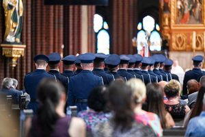 kolorowe zdjęcie wykonane z boku osób cywilnych znajdujących się w ławkach oraz policjantów kompani honorowej stojących w dwuszeregu