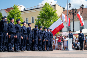 kolorowe zdjęcie stojących na baczność policjantów, w tle flaga RP