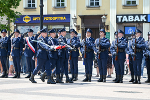 kolorowe zdjęcie policjantów Kompani Honorowej maszerujący z flagą RP oraz szablami, policjanci stojący w szeregu oddają honor