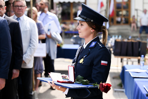 kolorowe zdjęcie przedstawiające uśmiechniętą policjantkę trzymającą w dłoni odznaczenie oraz róże