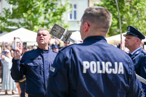kolorowe zdjęcie przedstawiające głowice sztandaru oraz policjanta unoszącego prawą dłoń do ślubowania