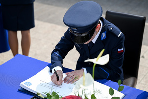 kolorowe zdjęcie przedstawiające policjanta składającego podpis na dokumencie