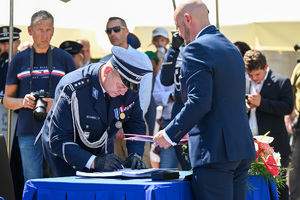 Kolorowe zdjęcie przedstawiające Oficera Policji składającego podpis na dokumencie